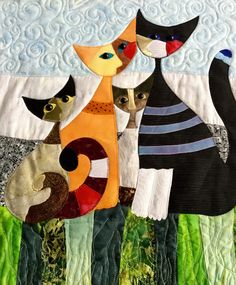 two cats are standing next to each other in front of a quilted wall hanging