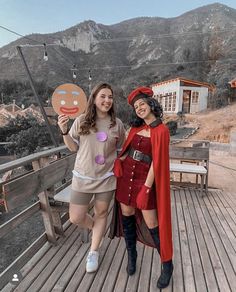 two women dressed in costumes posing for a photo on a wooden deck with mountains in the background