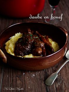 a wooden bowl filled with meat and mashed potatoes next to a glass of wine