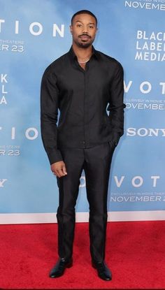 a man in a black suit standing on a red carpet with his hands in his pockets