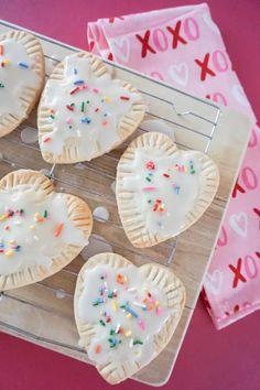 four heart shaped cookies sitting on top of a cooling rack with sprinkles