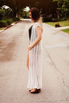 a woman is standing on the street wearing a long white crochet dress and sandals