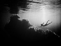 a black and white photo of a person swimming in the water with rocks underneath them