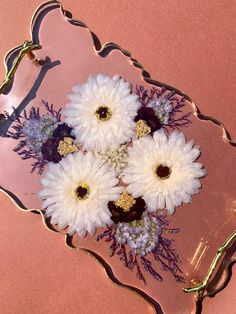 white and purple flowers are in a glass tray on a pink tablecloth with gold trim