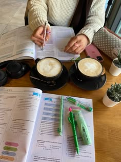 a woman is sitting at a table with two cups of coffee and an open book