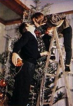 two people on a ladder decorating a christmas tree