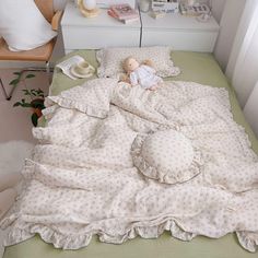 a small doll is laying on a bed with a blanket and pillows in the corner