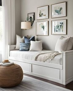 a white daybed with pillows and pictures on the wall above it in a living room