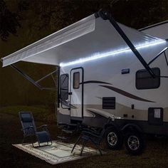 an rv parked in the grass at night with its lights on and a chair under it