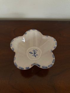 a white and blue flower shaped dish sitting on top of a wooden table next to a wall