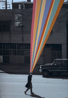 a person carrying a large colorful kite on their head while walking down the street in front of a black truck