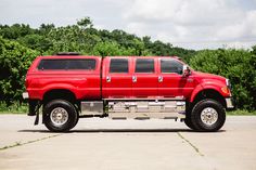 a red pick up truck parked in a parking lot next to some bushes and trees