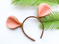 a pink mouse ears headband on top of a palm tree branch with green leaves