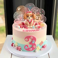 a pink and blue cake with a dog on it's top is sitting on a table