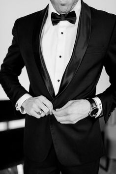 a man in a tuxedo is wearing a watch and looking at the camera