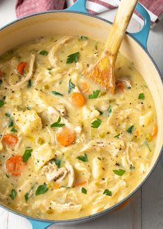 a pot filled with chicken noodle soup on top of a white table next to a wooden spoon