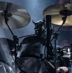 the drummer is playing drums on stage with his head in the drum kit and lighting behind him