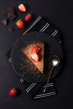 a piece of chocolate cake with strawberries on the side and two spoons next to it