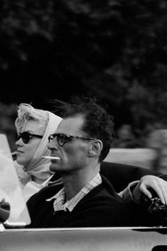 black and white photograph of two people sitting in a car with one woman wearing a headscarf