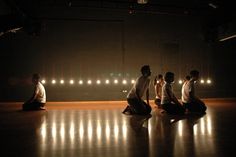 five people sitting on the floor in a dark room with their hands together as they talk