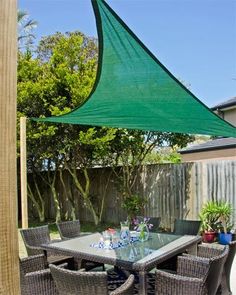 an outdoor dining area with table and chairs under a large green shade over the patio