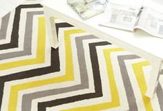 a yellow and gray chevroned rug sitting on top of a white table next to magazines