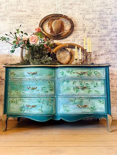 an old dresser painted in blue with flowers and birds on it, next to a brick wall