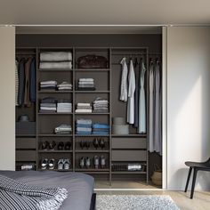 an open closet with clothes and shoes on shelves next to a bed in a bedroom