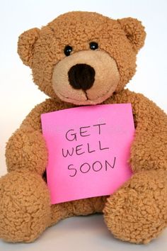 a teddy bear holding a pink sign that says get well soon on it's chest