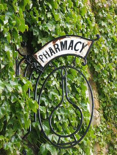 a sign that says pharmacy hanging from the side of a wall covered in ivys