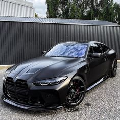 a black sports car is parked in front of a metal wall and trees on the other side