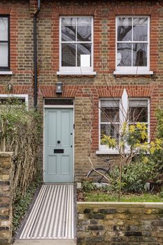 a blue door is in front of a brick building with white windows and green plants