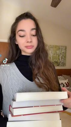 a young woman is holding several books in her hands and looking down at the camera