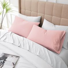 a bed with pink sheets and pillows on top of it next to a plant in a vase