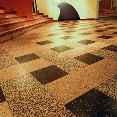 an empty room with black and white checkered flooring in front of a staircase