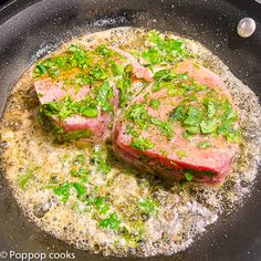 two pieces of meat in a frying pan with herbs on top and seasonings sprinkled over them