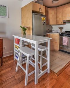 a kitchen with wooden floors and stainless steel appliances in the center, along with a dining table that has two stools on it