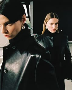 two women in black leather jackets standing next to each other and looking at the camera