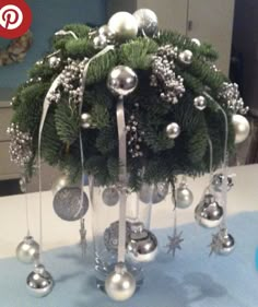 a christmas tree with silver ornaments and bells on it's top, sitting on a table in front of a mirror