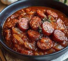 a close up of a bowl of food with sausages and onions in it on a wooden table