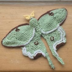 a crocheted green and brown butterfly sitting on top of a wooden table