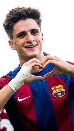 a man making a heart shape with his hands while standing in front of a soccer ball