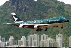 a large passenger jet flying over a city with tall buildings in the background and a mountain behind it