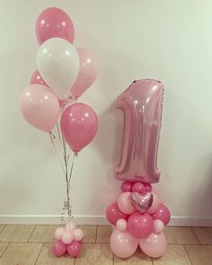 pink and white balloons with the number one on them are in front of a wall