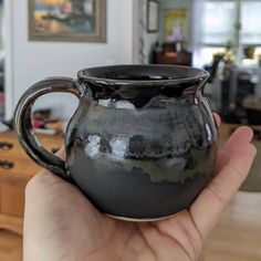 a hand holding a black ceramic mug in a living room