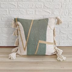 a green and white pillow with tassels on the bottom, sitting against a brick wall