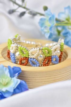 a close up of a bracelet on a wooden stand with flowers in the background and blue flowers