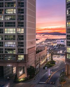 an aerial view of a city at sunset with the ocean and mountains in the background