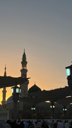 a group of people standing around in front of a building at sunset or dawn with the sun going down