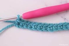 the crochet stitch is being worked on by a pink handled knitting needle,